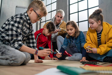 Eine Gruppe glücklicher Kinder mit ihrem Lehrer, die gemeinsam an einem Projekt im Klassenzimmer arbeiten. - HPIF02357