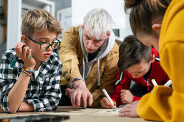 Eine Gruppe glücklicher Kinder mit ihrem Lehrer, die gemeinsam an einem Projekt im Klassenzimmer arbeiten. - HPIF02362