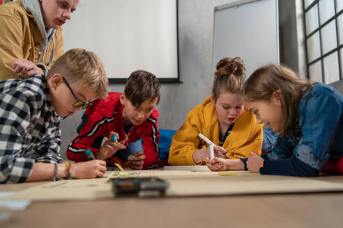 Eine Gruppe glücklicher Kinder mit ihrem Naturwissenschaftslehrer mit elektrischen Spielzeugen und Robotern im Robotik-Klassenzimmer - HPIF02363