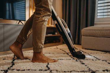 A lowsection of man hoovering carpet with vacuum cleaner in living room - HPIF02390