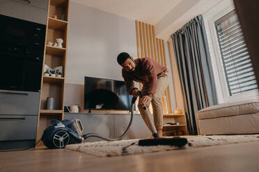 Ein junger Mann saugt den Teppich im Wohnzimmer mit einem Staubsauger - HPIF02392