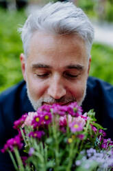 A portrait of happy mature businessman with flower bouquet sitting on bench and waiting for girlfriend. - HPIF02415