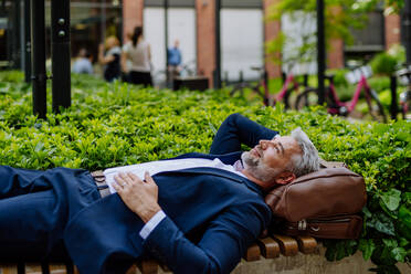 Ein reifer Geschäftsmann entspannt sich auf einer Bank im Stadtpark während einer Arbeitspause, Work-Life-Balance-Konzept. - HPIF02416