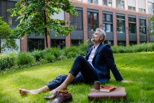 A mature businessman resting and sitting barefoot in park, feeling free, escaping from work, work life balance concept. - HPIF02434