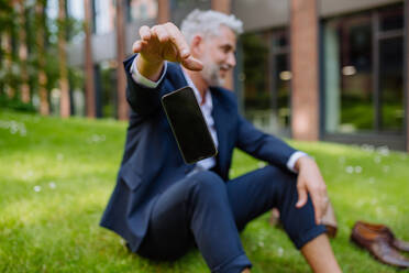 Ein reifer Geschäftsmann, der sein Smartphone wegwirft, wenn er barfuß im Park sitzt, sich frei fühlt und dem Arbeitsgedanken entflieht. - HPIF02435