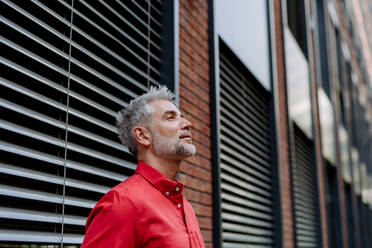 A mature businessman standing on street in front of window with blinders, copy space. - HPIF02439