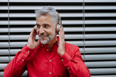 Ein reifer Geschäftsmann, der während einer Arbeitspause auf dem Balkon Musik mit Kopfhörern genießt. - HPIF02441