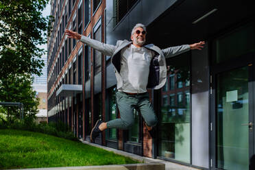 A fun portrait of happy energetic mature businessman with arms outstretched balancing on wall , feeling free, work life balance concept. - HPIF02448