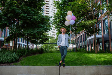 A fun portrait of happy energetic mature businessman holding balloons and walking on wall , feeling free, work life balance concept. - HPIF02453