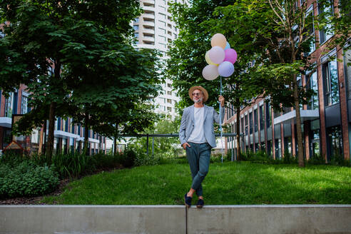 A fun portrait of happy energetic mature businessman holding balloons and walking on wall , feeling free, work life balance concept. - HPIF02453