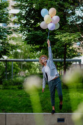 A fun portrait of happy energetic mature businessman holding balloons and walking on wall , feeling free, work life balance concept. - HPIF02454