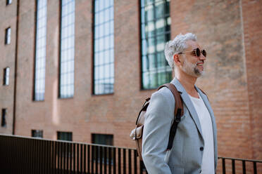 A confident man wearing backpack walking in street, businessman in casual clothes in summer on the way to work. - HPIF02468