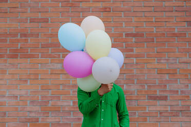 A fun portrait of happy energetic mature man holding balloons in street and hiding behind them, feeling free. - HPIF02480