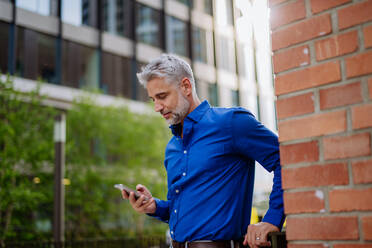 A successful happy businessman waiting in city street, using mobile phone, commuting concept. - HPIF02496