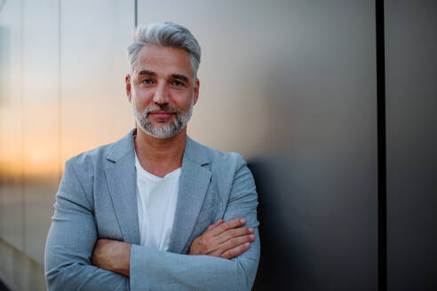 A mature relaxed businessman leaning on street wall, work life balance concept. - HPIF02533