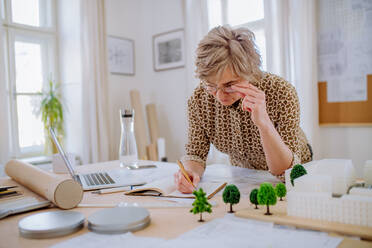 A senior woman eco architect with model of modern bulidings working in office. - HPIF02569