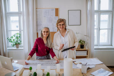 Reife Architektinnen arbeiten zusammen in einem Büro und schauen in die Kamera. - HPIF02596
