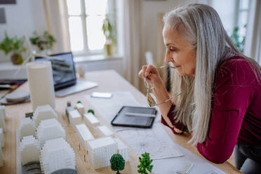 A senior woman eco architect with model of modern bulidings working in office. - HPIF02611