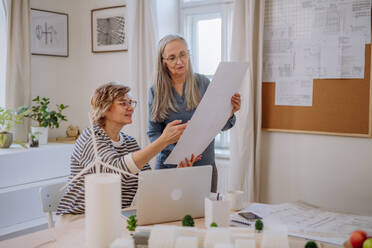 Mature women eco architects with model of modern bulidings and blueprints working together in an office. - HPIF02615