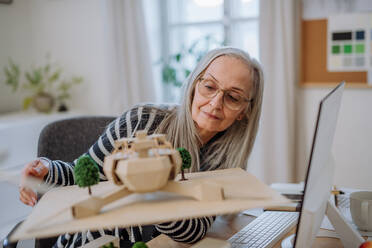 Eine ältere Architektin hält ein Modell eines modernen Ökobaus im Büro - HPIF02629
