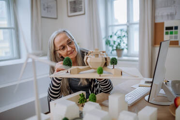 A senior woman architect holding model of modern eco buliding in office - HPIF02630