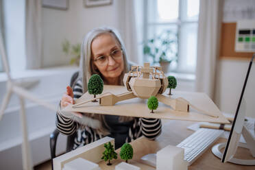 A senior woman architect holding model of modern eco buliding in office - HPIF02631