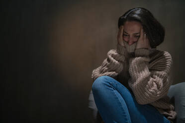 A depressed mid-adult woman sitting on the floor in the dark and crying. - HPIF02658