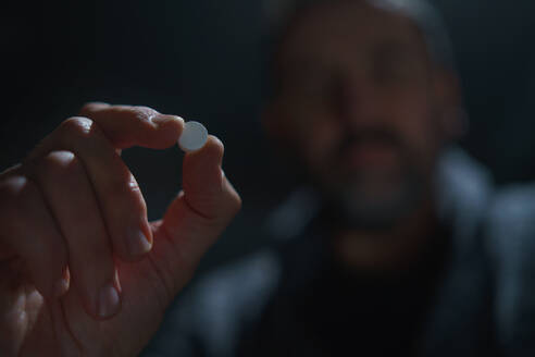 Eine unscharfe Mann hält und zeigen Droge Pille auf dunklem Hintergrund, psychische Gesundheit Konzept. - HPIF02665
