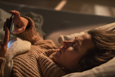 Eine traurige Frau, die nachts im Bett liegend ihr Smartphone benutzt, Konzept der Technologiesucht und Schlaflosigkeit. - HPIF02688