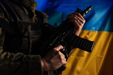 Nahaufnahme eines Soldaten in Militäruniform, der eine Waffe hält, mit der Flagge der Ukraine im Hintergrund. - HPIF02767