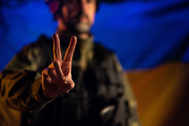 Ein Soldat in Militäruniform zeigt ein Friedenszeichen mit der Flagge der Ukraine im Hintergrund. - HPIF02770