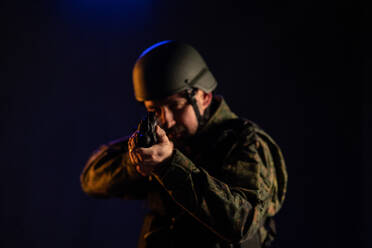 Ein Soldat in Militäruniform und Helm zielt mit der Waffe auf die Kamera auf schwarzem Hintergrund. - HPIF02771