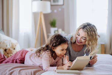 Eine glückliche Mutter mit ihrer kleinen Tochter, die zu Hause auf dem Bett liegt und ein Buch liest. - HPIF02866