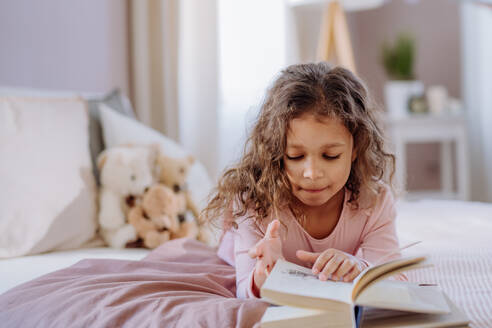 A little girl lying on bed and reading book at home. - HPIF02867