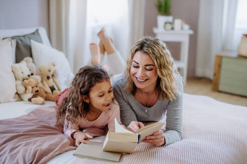 Eine glückliche Mutter mit ihrer kleinen Tochter, die zu Hause auf dem Bett liegt und ein Buch liest. - HPIF02868