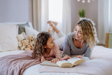 A happy mother with her little daughter lying on bed and reading book at home. - HPIF02869