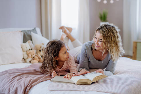 Eine glückliche Mutter mit ihrer kleinen Tochter, die zu Hause auf dem Bett liegt und ein Buch liest. - HPIF02869