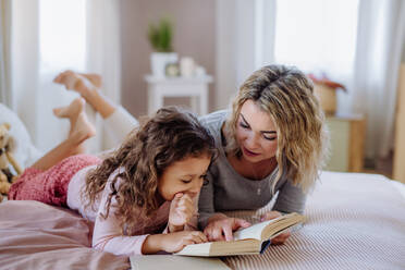 Eine glückliche Mutter mit ihrer kleinen Tochter, die zu Hause auf dem Bett liegt und ein Buch liest. - HPIF02870