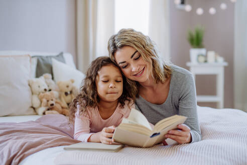 Eine glückliche Mutter mit ihrer kleinen Tochter, die zu Hause auf dem Bett liegt und ein Buch liest. - HPIF02871