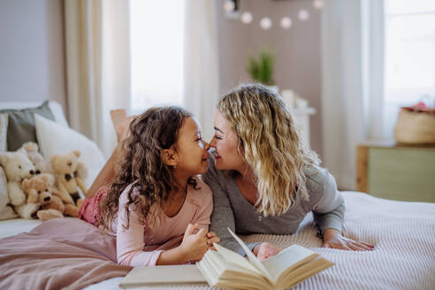 Eine glückliche Mutter und ihre kleine Tochter liegen auf dem Bett und sehen sich beim Lesen eines Buches an. - HPIF02872
