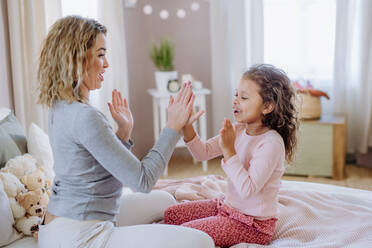 Eine glückliche Mutter mit ihrer kleinen Tochter spielt klatschende Hände Spiel auf dem Bett zu Hause. - HPIF02873