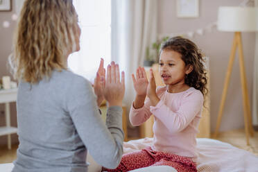 A happy mother with her little daughte playing clapping hands game on bed at home. - HPIF02874