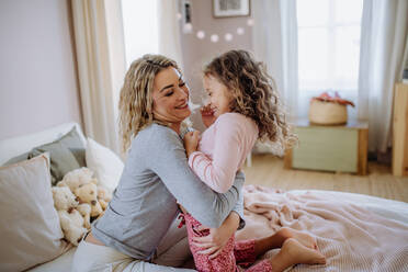 Eine glückliche Mutter mit ihrer kleinen Tochter, die sich umarmen und gemeinsam Spaß im Bett zu Hause haben. - HPIF02880