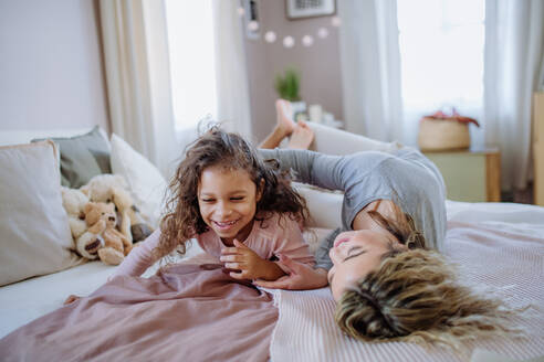 Eine glückliche Mutter mit ihrer kleinen Tochter, die sich umarmen und gemeinsam Spaß im Bett zu Hause haben. - HPIF02881