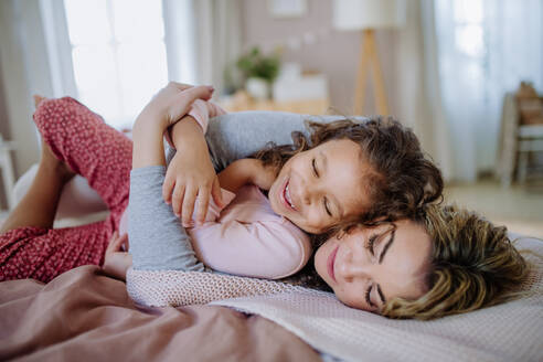 Eine glückliche Mutter, die mit ihrer kleinen Tochter im Bett liegt und es sich zu Hause gemütlich macht. - HPIF02882