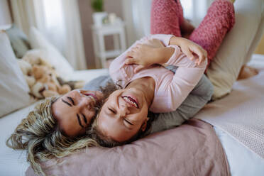 Eine glückliche Mutter mit ihrer kleinen Tochter, die sich umarmen und gemeinsam Spaß im Bett zu Hause haben. - HPIF02883