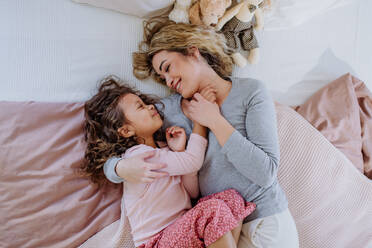 An overhead view of mid adult mother lying on bed with her little daughter at home. - HPIF02884