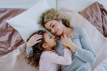 Blick von oben auf eine erwachsene Mutter, die mit ihrer kleinen Tochter zu Hause auf dem Bett liegt. - HPIF02885