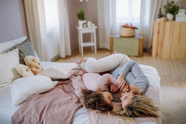 Eine glückliche Mutter und ihre kleine Tochter liegen zusammen auf dem Bett und schauen sich an. - HPIF02886