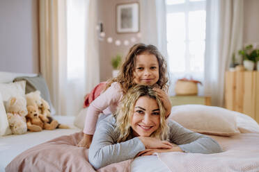 Ein glückliches kleines Mädchen, das auf dem Rücken seiner Mutter im Bett liegt und in die Kamera schaut. - HPIF02887